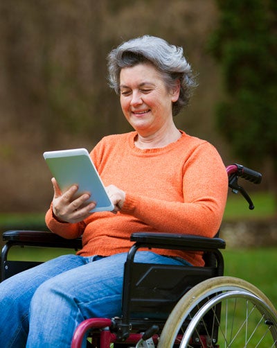 woman in wheelchair holding and looking at tablet computer